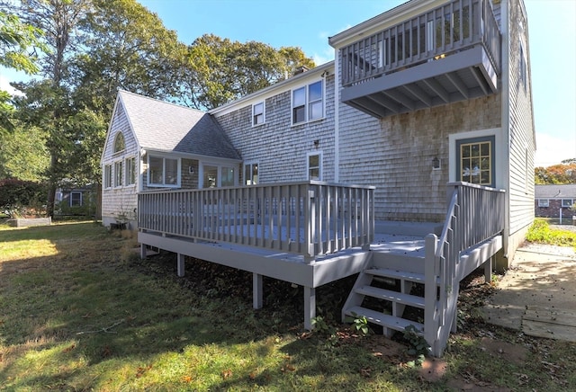 rear view of house with a balcony, a wooden deck, and a lawn