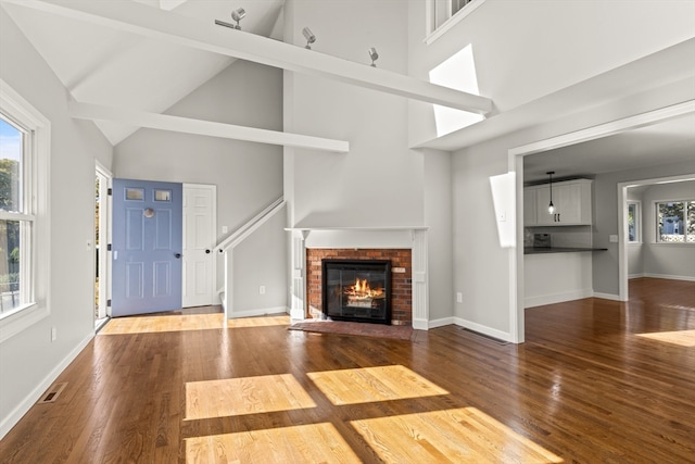 unfurnished living room featuring wood-type flooring, a fireplace, beam ceiling, and high vaulted ceiling