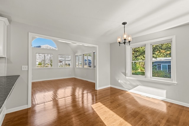 unfurnished dining area featuring a notable chandelier, a wealth of natural light, and hardwood / wood-style floors