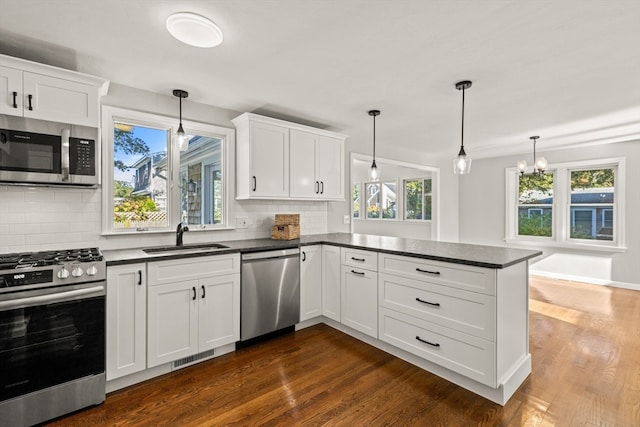 kitchen with appliances with stainless steel finishes, kitchen peninsula, decorative light fixtures, and sink