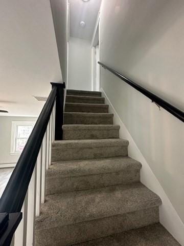 stairs featuring a baseboard heating unit and carpet floors