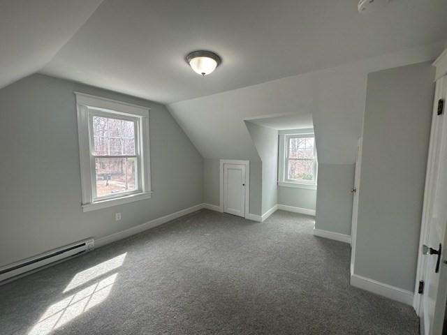 additional living space featuring baseboard heating, dark colored carpet, baseboards, and vaulted ceiling