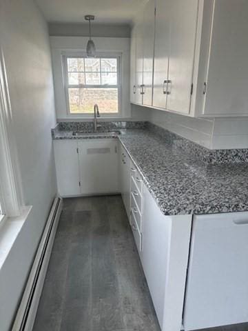 kitchen with baseboard heating, stone countertops, white cabinetry, and a sink