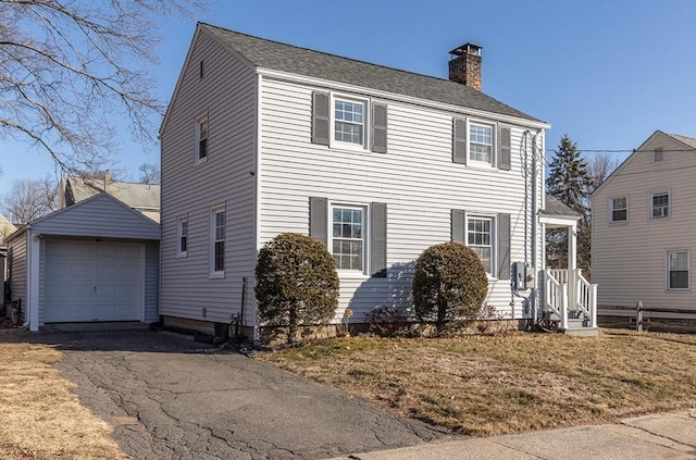 colonial-style house with an outbuilding, aphalt driveway, a detached garage, and a chimney