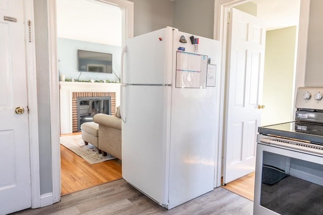 kitchen featuring a brick fireplace, light wood-style flooring, freestanding refrigerator, and electric stove