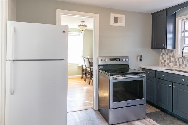 kitchen with decorative backsplash, light wood-style flooring, freestanding refrigerator, electric stove, and a sink