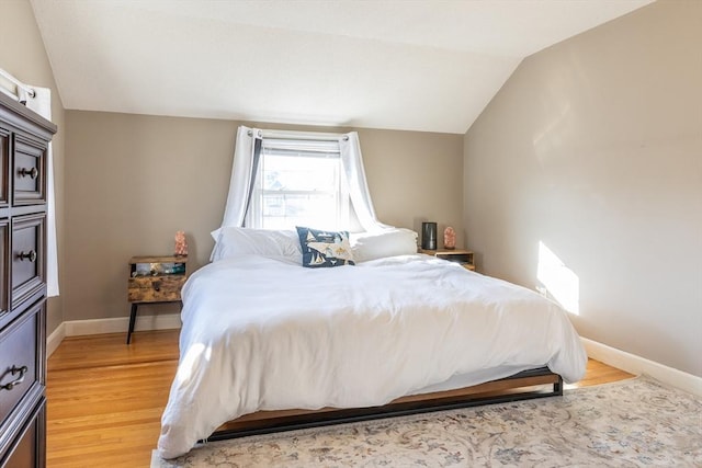 bedroom featuring light wood-type flooring, lofted ceiling, and baseboards