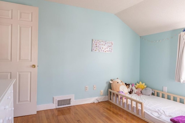 unfurnished bedroom featuring visible vents, lofted ceiling, baseboards, and wood finished floors