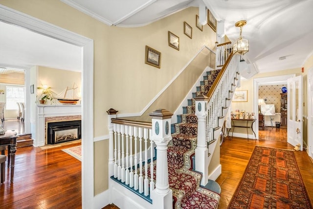 stairs with wood-type flooring, a fireplace with flush hearth, a chandelier, baseboards, and ornamental molding
