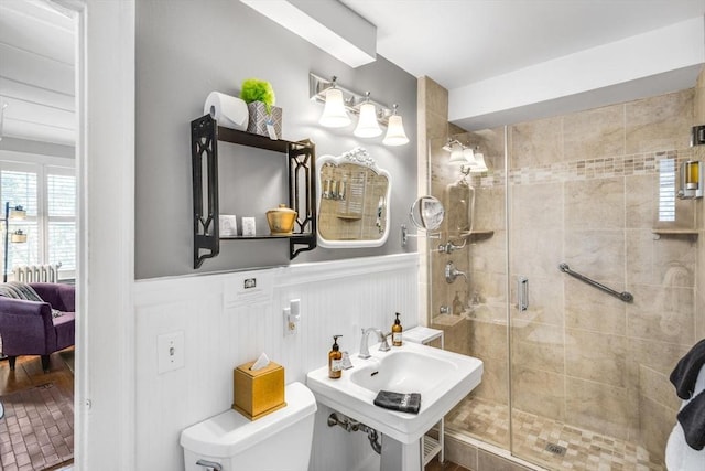 ensuite bathroom with a wainscoted wall, a shower stall, toilet, a decorative wall, and a sink