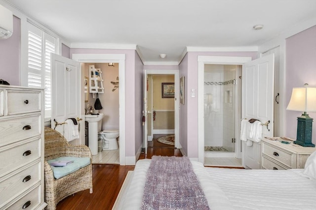 bedroom with ensuite bath, ornamental molding, dark wood finished floors, baseboards, and an AC wall unit