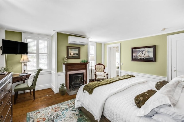 bedroom with a wall mounted AC, wood finished floors, a fireplace with raised hearth, crown molding, and baseboards
