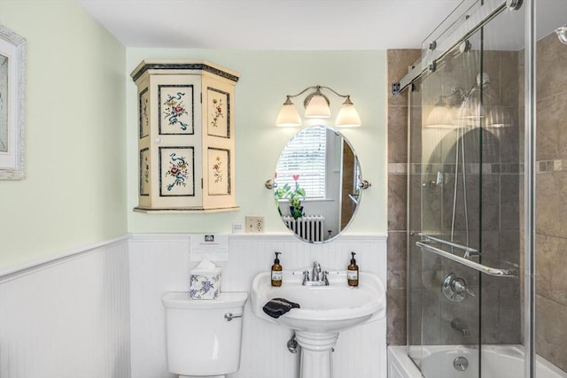 full bath with wainscoting, toilet, shower / bath combination with glass door, and a sink