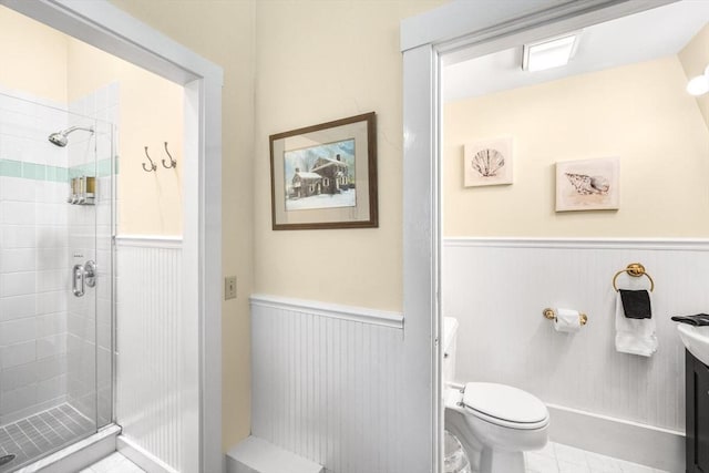 bathroom featuring a wainscoted wall, a stall shower, tile patterned floors, and toilet