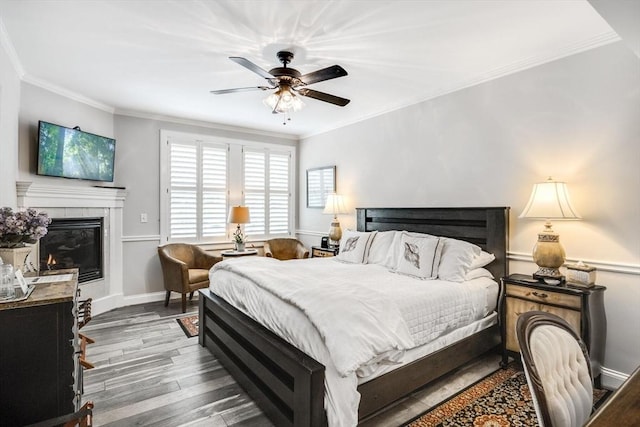 bedroom with a tile fireplace, wood finished floors, ornamental molding, a ceiling fan, and baseboards