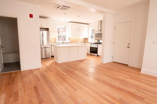 8 Brookside Ave Unit 2, Boston, MA 02130 - kitchen featuring appliances with stainless steel finishes, wall chimney range hood, a sink, white cabinetry, and light wood finished floors