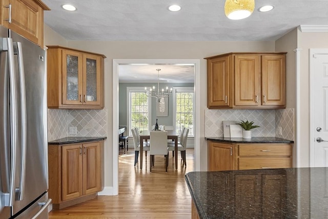 kitchen with backsplash, freestanding refrigerator, dark stone countertops, glass insert cabinets, and light wood-style flooring