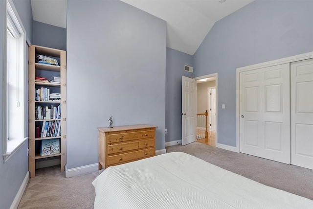 bedroom featuring visible vents, a closet, vaulted ceiling, and light carpet