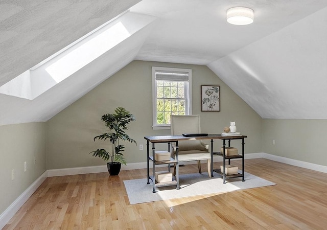 home office with vaulted ceiling with skylight, baseboards, and wood finished floors
