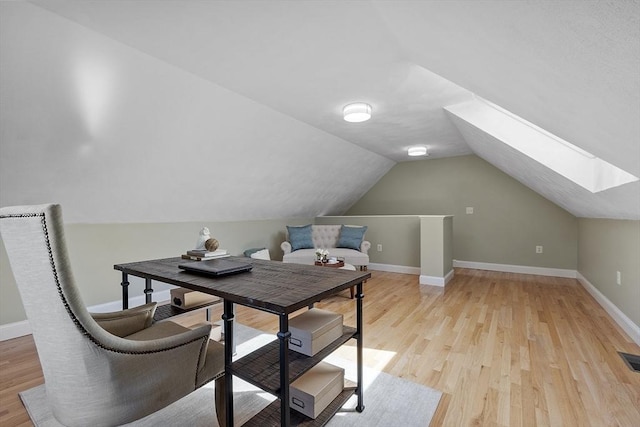 office area with baseboards, visible vents, lofted ceiling with skylight, and light wood-style floors