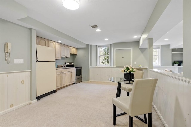 kitchen featuring visible vents, freestanding refrigerator, electric range, light brown cabinetry, and a wainscoted wall