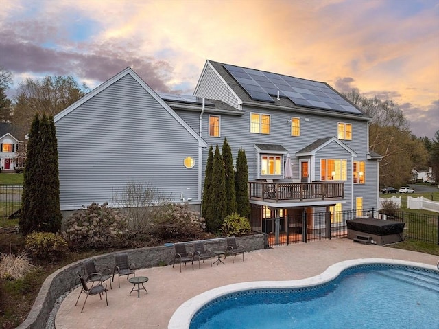 back of property at dusk featuring fence, roof mounted solar panels, a fenced in pool, and a patio area