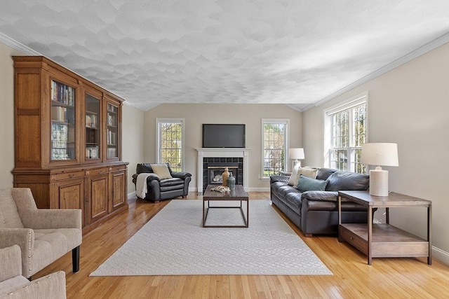 living room featuring crown molding, lofted ceiling, a fireplace, baseboards, and light wood-type flooring