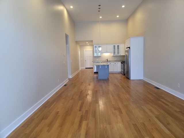 kitchen featuring pendant lighting, light hardwood / wood-style flooring, appliances with stainless steel finishes, white cabinets, and a kitchen island