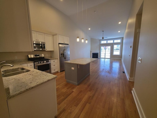 kitchen featuring a center island, appliances with stainless steel finishes, pendant lighting, light stone countertops, and white cabinets