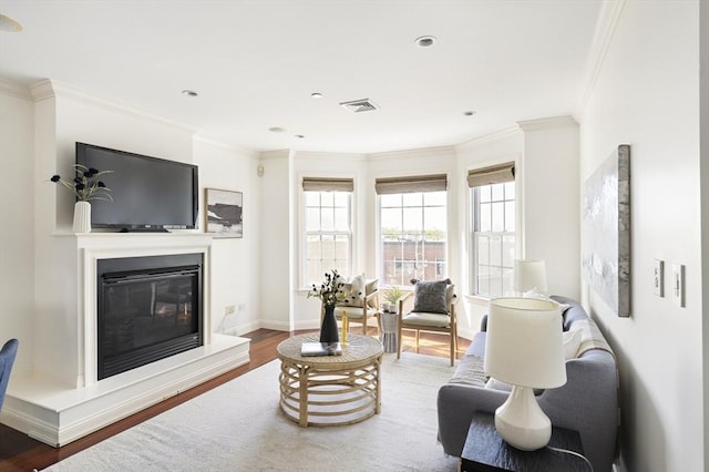 living room with baseboards, ornamental molding, a glass covered fireplace, visible vents, and wood finished floors