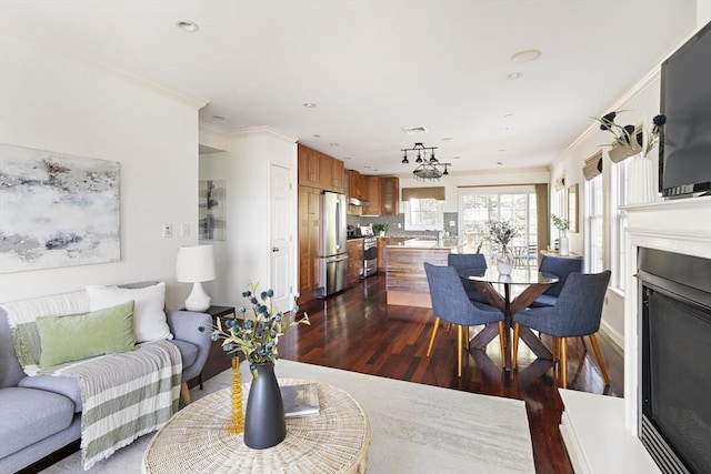 living room with dark wood-type flooring, visible vents, ornamental molding, and a glass covered fireplace