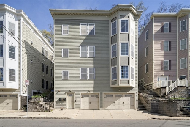 view of property with stairway, an attached garage, and driveway