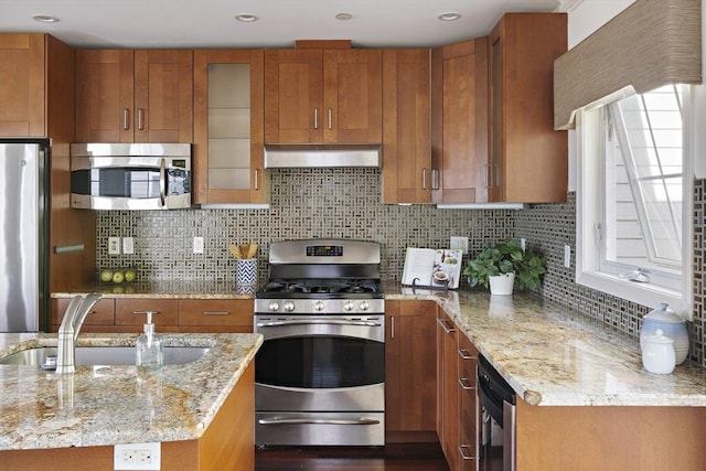 kitchen with appliances with stainless steel finishes, brown cabinetry, wall chimney exhaust hood, and a sink
