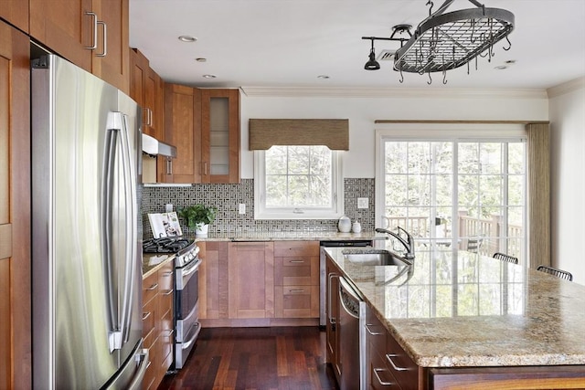 kitchen featuring a sink, a kitchen island with sink, light stone countertops, backsplash, and appliances with stainless steel finishes