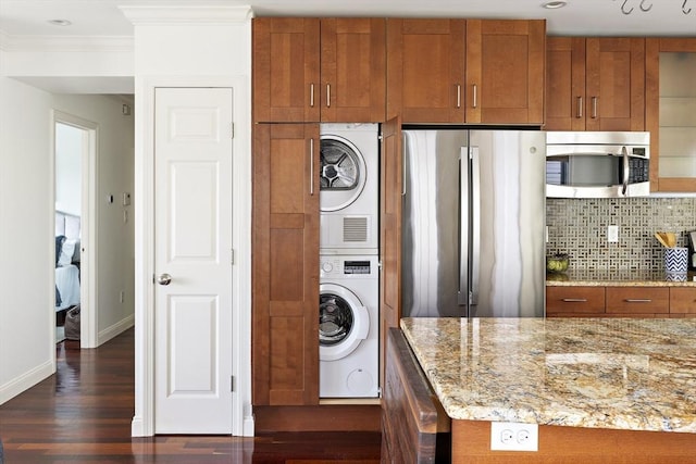 kitchen featuring stacked washer and clothes dryer, stainless steel appliances, brown cabinets, and dark wood-style floors