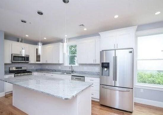 kitchen with white cabinets, appliances with stainless steel finishes, a kitchen island, and pendant lighting