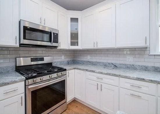 kitchen featuring white cabinets, backsplash, stainless steel appliances, and light stone countertops