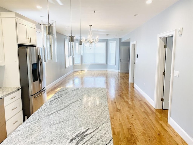 kitchen featuring pendant lighting, white cabinets, light wood-type flooring, light stone counters, and stainless steel fridge with ice dispenser