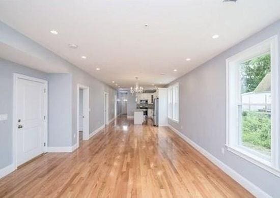 unfurnished living room featuring a chandelier, light wood-type flooring, and plenty of natural light