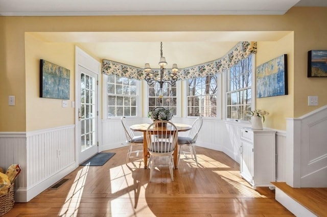 dining space with light wood finished floors, a wainscoted wall, visible vents, and an inviting chandelier