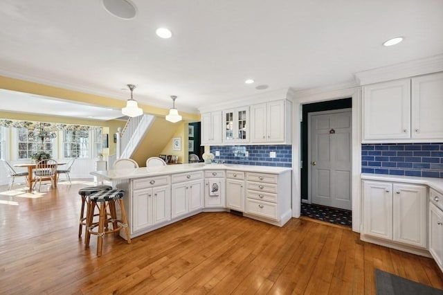 kitchen with a breakfast bar, a peninsula, light countertops, white cabinets, and light wood-type flooring