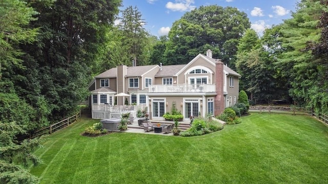 rear view of house with a yard, a balcony, a chimney, and french doors