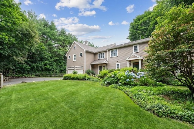 colonial-style house with driveway, an attached garage, a front lawn, and fence