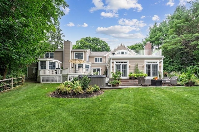 rear view of house featuring fence, a yard, a chimney, a hot tub, and a deck