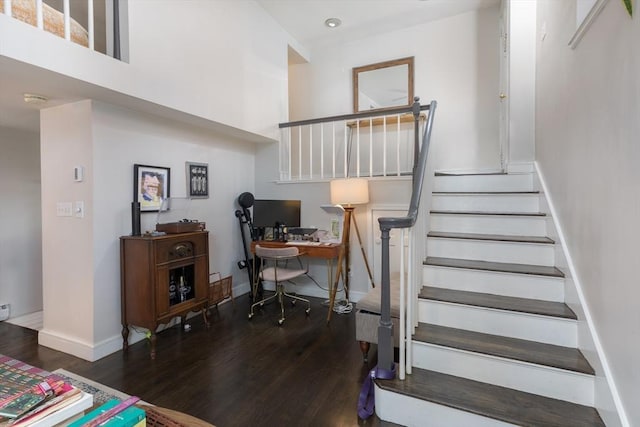 staircase with wood finished floors, baseboards, and a towering ceiling
