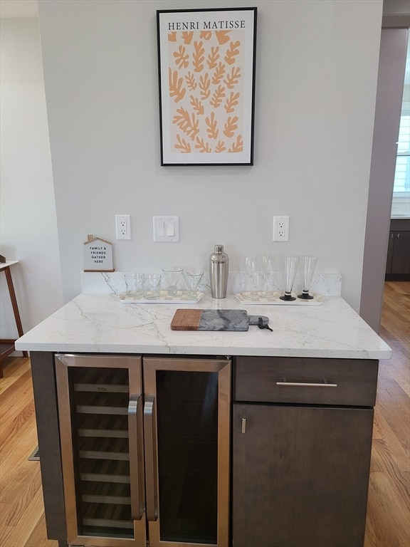 bar featuring dark brown cabinetry, wine cooler, light stone counters, and light hardwood / wood-style flooring