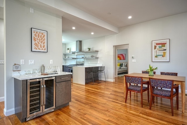 kitchen with wine cooler, high end range, dark brown cabinetry, light hardwood / wood-style floors, and wall chimney range hood