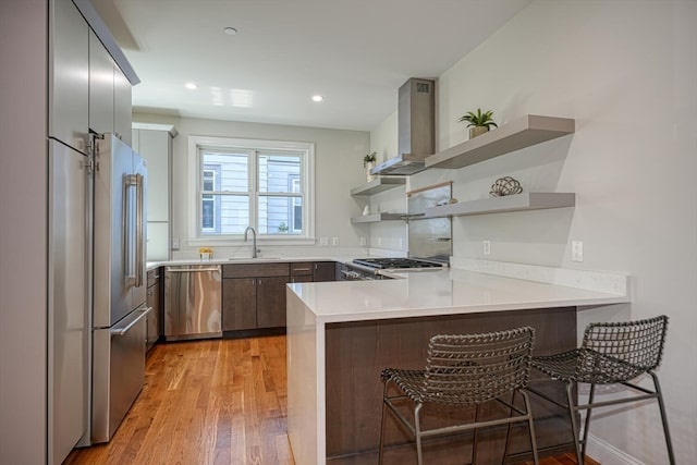 kitchen with appliances with stainless steel finishes, sink, a breakfast bar area, kitchen peninsula, and wall chimney range hood