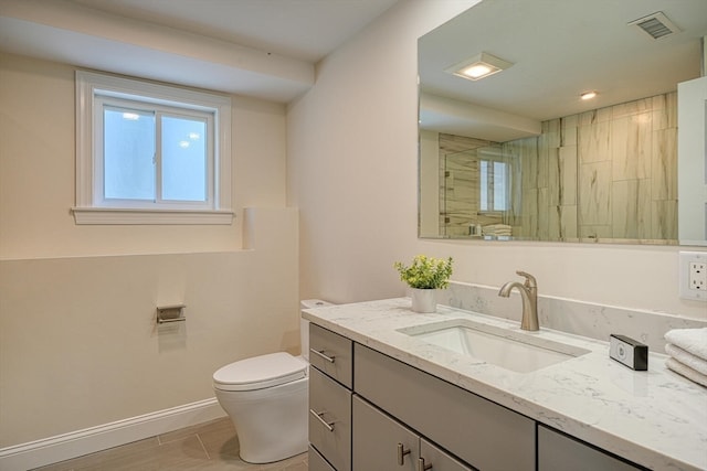 bathroom with tiled shower, vanity, and toilet