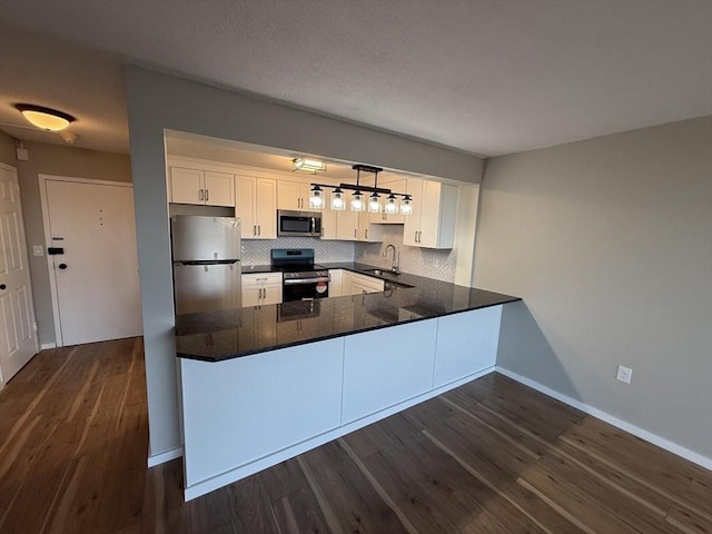 kitchen featuring kitchen peninsula, appliances with stainless steel finishes, sink, white cabinets, and hanging light fixtures